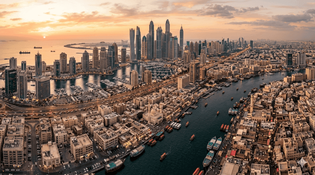 Panoramic aerial view of Dubai showing contrasting neighborhoods from the traditional Creek area to modern Marina skyline at golden hour